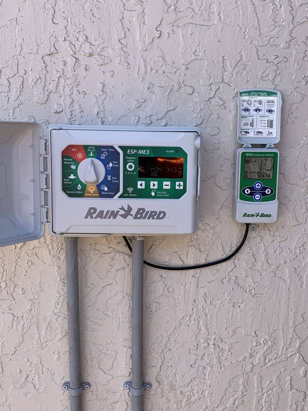 A Rain Bird smart controller with a wireless rain sensor mounted above it