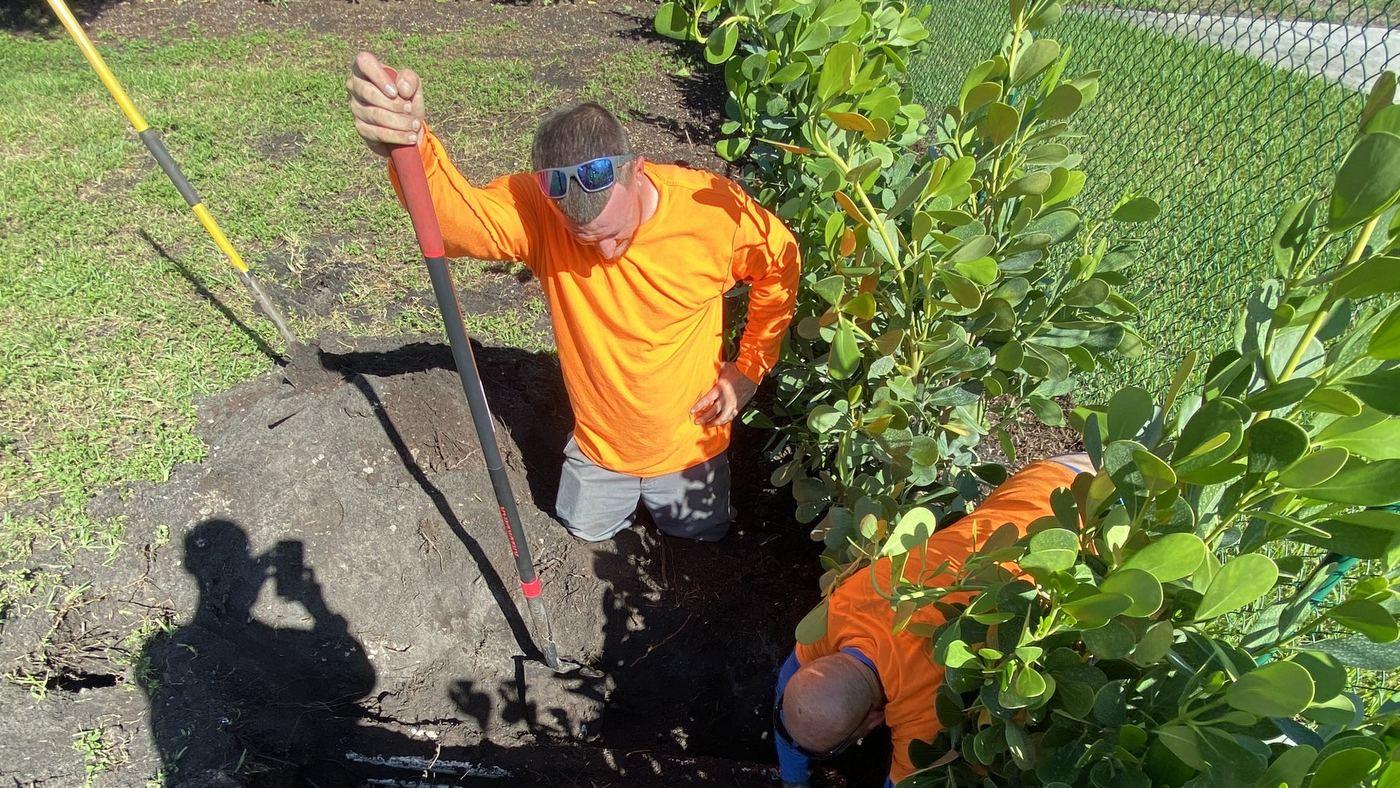 Expert Irrigation crew trenching along a hedge line in Broward County